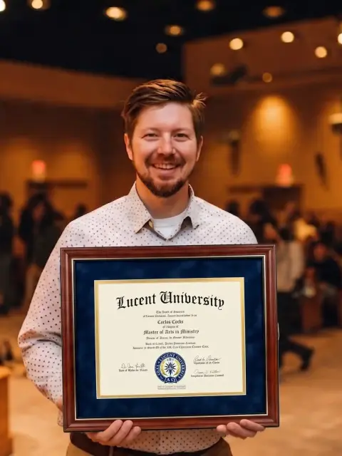 Lucent University bachelor's graduate holding his diploma in church